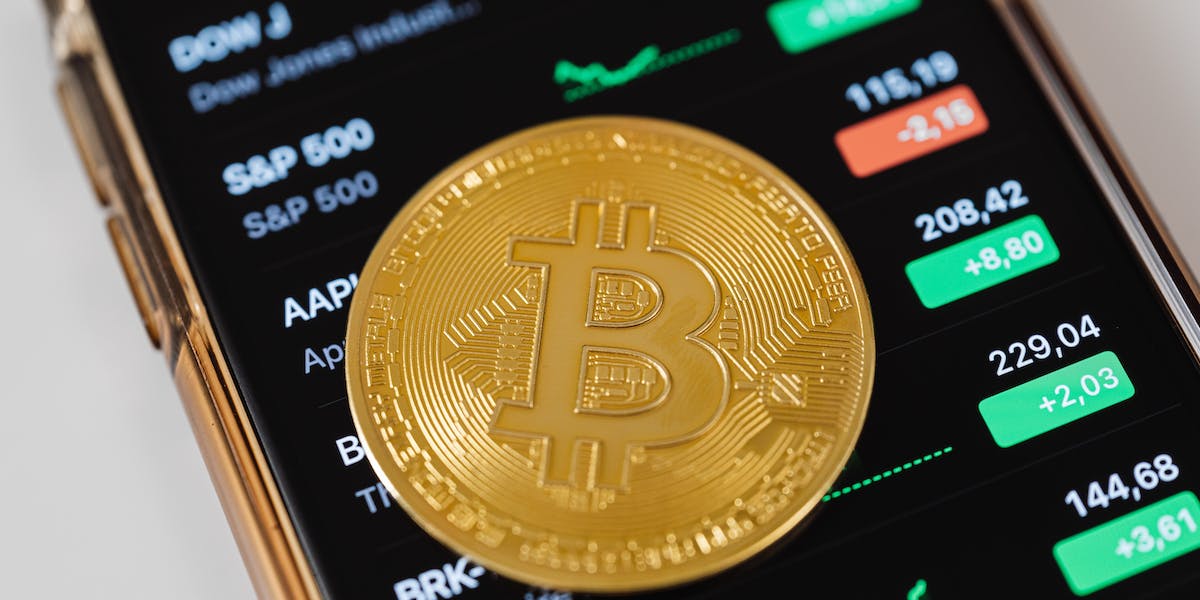 Bitcoin-coin-rests-on-mobile-phone-with-list-of-trading-tickets.